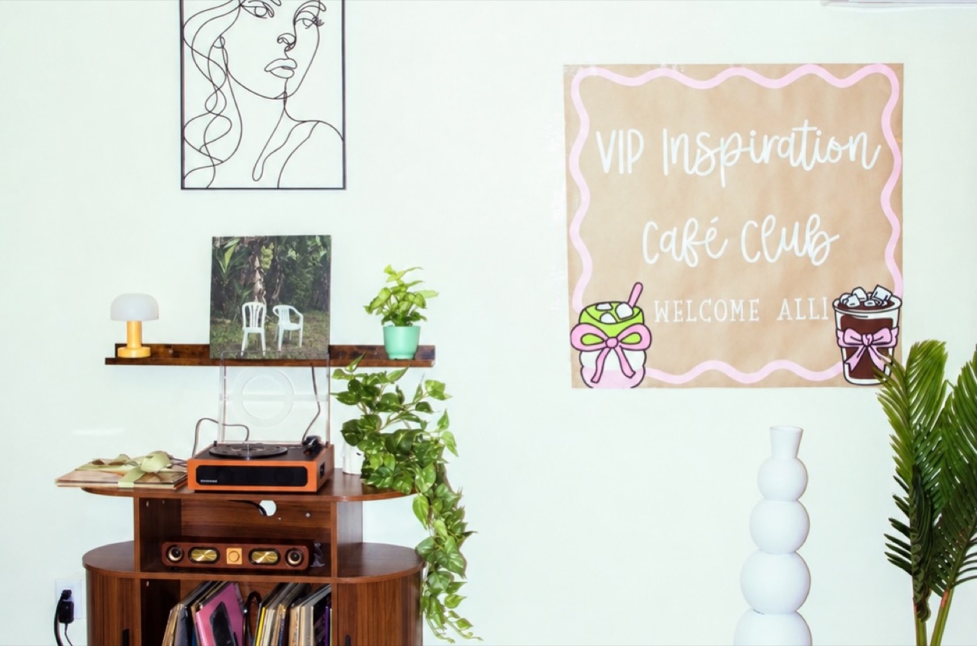 Line-drawing art on the wall above a record player and a shelf of plants
